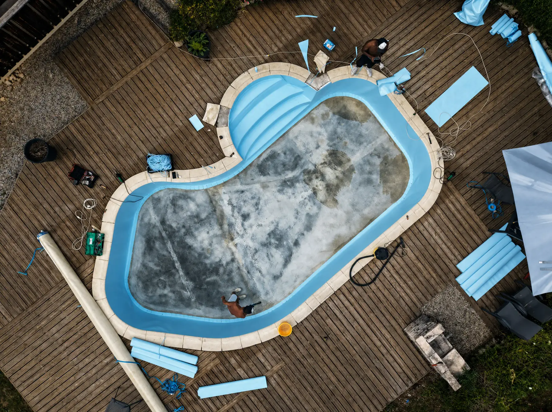 Vue drone d'une piscine forme haricot en cours de rénovation, lés de membrane bleu clair posés sur une partie du bassin
